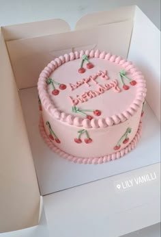 a pink birthday cake with cherries on it sitting in a box for someone to eat