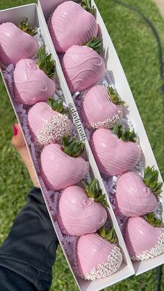 a person holding two boxes filled with pink chocolate covered strawberries on top of green grass