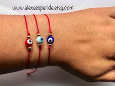 These beautifully handmade bracelets are made of nylon thread, small gold plated beads and a glass Turkish (evil) eye bead. They are made with either brown, white or red thread and are tied with a sliding knot to adjust and fit most writs. These are a great accessory for everyday wear. They are great for spiritual and evil eye purposes. You can choose the color of the thread for your bracelets and the color of the glass eye beads. We are sure you will love these bracelets! Estas pulseras hechas Eye Round, Turkish Evil Eye, Red Thread, Eye Beads, Sliding Knot, Glass Eyes, Beauty Supply, Beauty Trends, Organza Bags