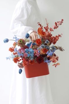 a woman holding a red bucket filled with flowers