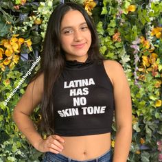 a woman standing in front of a green wall wearing a black crop top with latina has no skin tone written on it