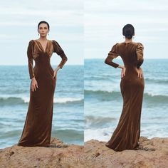 a woman standing on top of a rock next to the ocean wearing a brown dress