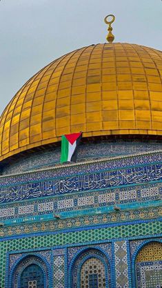 an ornate dome with a flag hanging from it's side in front of a blue and gold building