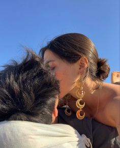 a man and woman kissing each other while sitting on top of a beach with the sky in the background