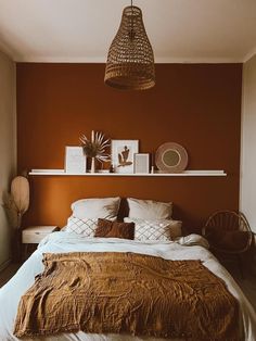 a bedroom with an orange wall and white bedding, wicker hanging from the ceiling