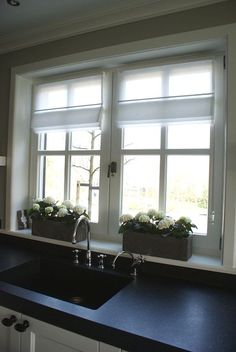 a kitchen sink sitting under two windows next to a window with white flowers in it