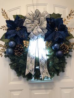 a wreath with blue poinsettis and pine cones hanging on the front door