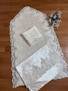 two pieces of white lace on top of a wooden floor next to a vase with flowers