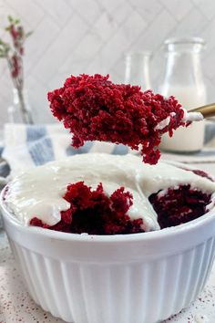 red velvet cake in a white bowl being spooned with cream cheese frosting on top