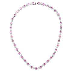 The timeless elegance of this tennis setting converges with rich pink sapphires to create a breathtakingly elegant design. Crafted in sterling silver, round-cut pink sapphires are prong set in a halo of created white sapphires with created white sapphire flower clusters connecting each pink sapphire. Glistering pink sapphires embezzle your neck with this timeless, royal design. Finished with an SL logo and a Suzy Levian Secret Signature brown diamond in the back gallery, this necklace is designe Elegant Pink Diamond Necklace With Accents, Pink Diamond Necklace For Formal Occasions, Formal Pink Diamond Necklace, Pink Oval Jewelry With Single Cut Diamonds, Oval Pink Jewelry With Single Cut Diamonds, Luxury Pink Diamond Necklace, Elegant Round Gemstone Tennis Necklace, Elegant Gemstone Tennis Necklace, Fine Pink Sapphire Necklaces For Formal Occasions