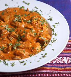 a white plate topped with meat covered in sauce and garnished with parsley