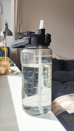 a water bottle sitting on top of a white table next to a bed and window