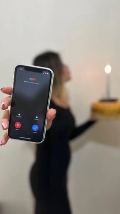 a woman holding up a cell phone in front of a cake with candles on it