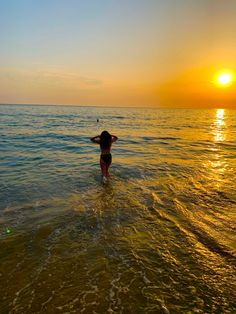 a woman standing in the ocean at sunset