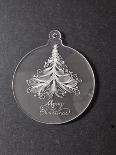 a glass ornament with a christmas tree on the bottom and merry christmas written in white