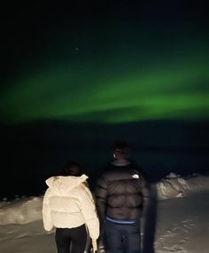 two people are standing in the snow looking at the aurora bore, or northern lights