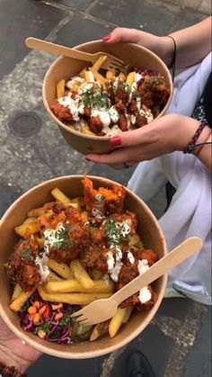 two people holding bowls filled with food on top of a street side walk next to each other