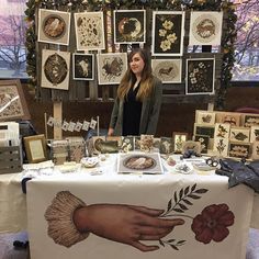 a woman standing in front of a table covered with pictures and cards at an art show