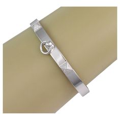 This stunning Collier de Chein collection is by Hermes, it features an authentic bangle crafted from 18k white gold with a high polished finish featuring a 6mm wide band. The front of the bangle has two small pyramid like design set with diamond and the center has a door knocker ring dangling below. It is signed by the designer with the serial number, gold content and diamond weight. Comes with Hermes box Brand: Hermes Hallmark: Au750 Hermes SH Made in France 16A087147 48D0.24ct Diamond: 0.24ct (48 diamonds) Material: 18k white gold Measurement: inner circumference: 6.25" x 0.23" wide Front: 1.75" across x 0.23" wide x 0.22" high Weight: 25.1 grams Hermes Bracelet, White Gold Bangle, Hermes Box, Door Knocker, Fine Jewelry Bracelets, Gold Bangle Bracelet, Gold Bangle, Design Set, Wide Bands