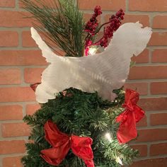 a white dog is sitting on top of a christmas tree decorated with red bows and greenery