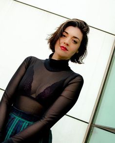 a woman standing in front of a white wall wearing a black top and green skirt