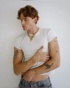 a man with tattoos on his arms and chest standing in front of a white wall