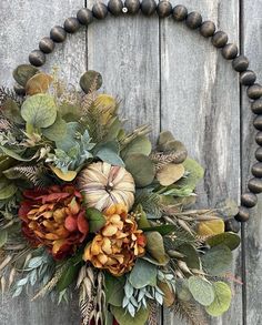 a wreath made out of leaves and flowers is hanging on a wooden door with a bead necklace around it