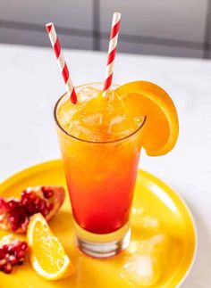 an orange drink on a yellow plate with two straws and pomegranate