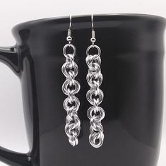 a pair of silver earrings sitting on top of a black coffee cup in front of a mug