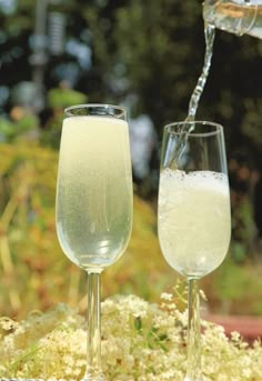 two wine glasses filled with white liquid being poured into one glass and another full to the side