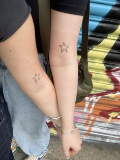 two people holding hands with small stars on their wrist tattooing one another's arm