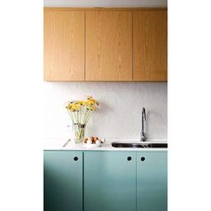 a kitchen with green cabinets and white counter tops, yellow flowers in the sink area