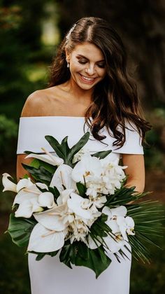 a woman in a white dress holding a bouquet of flowers and smiling at the camera