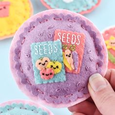 someone is holding up a small felt brooch that has seeds on it and other items in the background