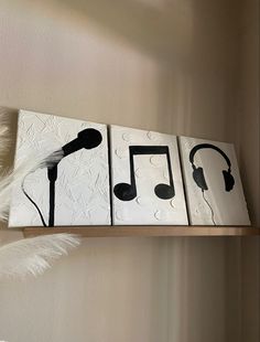 three canvases with music notes and headphones hanging on a wall next to a feather