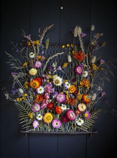 a bunch of flowers that are sitting on a shelf in front of a wall with a wire fence