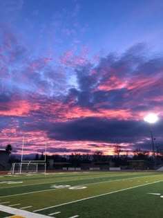 the sun is setting over a football field with clouds in the sky and grass on the ground