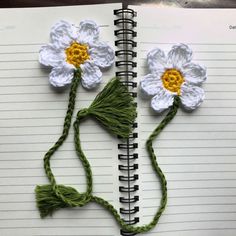 two crocheted flowers sitting on top of an open spiral bound note book with string