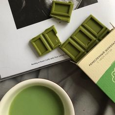 a cup of green tea next to a book and some chocolates on a table