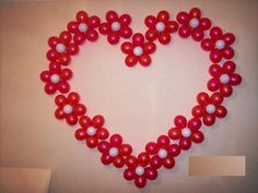 a heart made out of red and white balloons in the shape of flowers on a wall