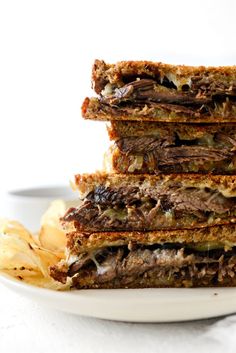 a stack of four sandwiches sitting on top of a white plate next to potato wedges