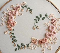 an embroidery project with pink flowers and green leaves on white fabric in a circular frame