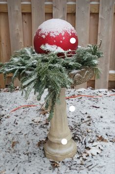 a red and white ball sitting on top of a cement vase filled with snow covered plants