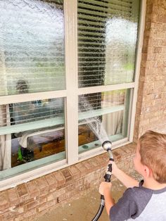 a young boy is spraying water out of a window with a sprayer in front of him