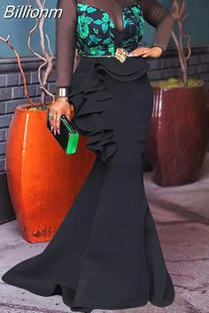 a woman in a black and green dress standing next to an orange potted plant