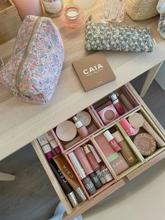 an open drawer with cosmetics and other items on it sitting on a table next to a purse