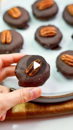 a hand holding a chocolate covered donut with pecans on top and another one in the background