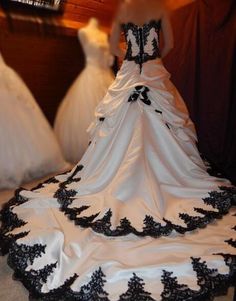 a wedding dress is displayed in front of two other gowns, one with black and white trim