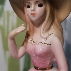 a porcelain figurine wearing a pink dress and hat with her hands on her hips