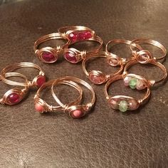 six rings with different colored stones are sitting on a leather surface, one is gold and the other is silver